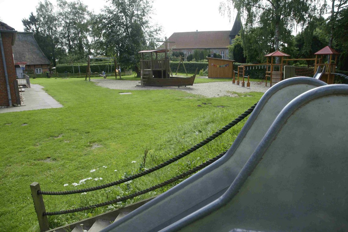 Rutsche im Vordergrund, im Hintergrund Überblick über das Außengelände mit Rutsche, Klettermöglichkeiten und Sandkasten