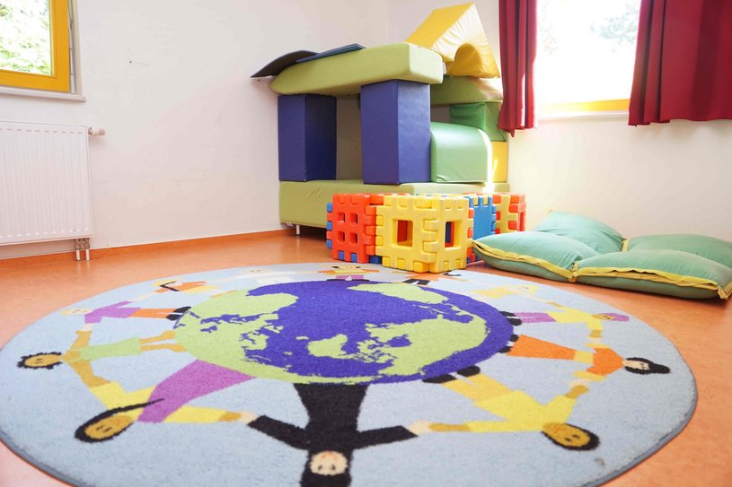 Bunter Spielteppich, im Hintergrund ein Haus aus Schaumstoff