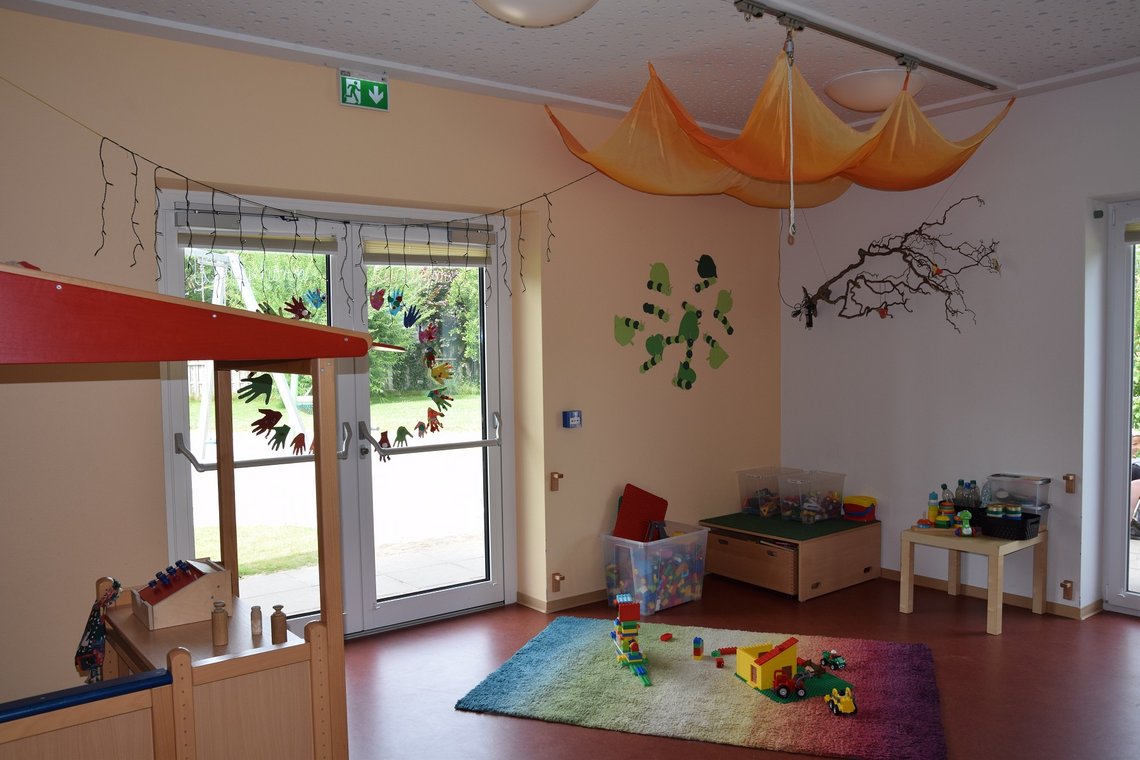 Kaufladen links, Spielteppich, darüber ein hellgelber Tuch-Himmel, im Hintergrund Spielzeugkisten