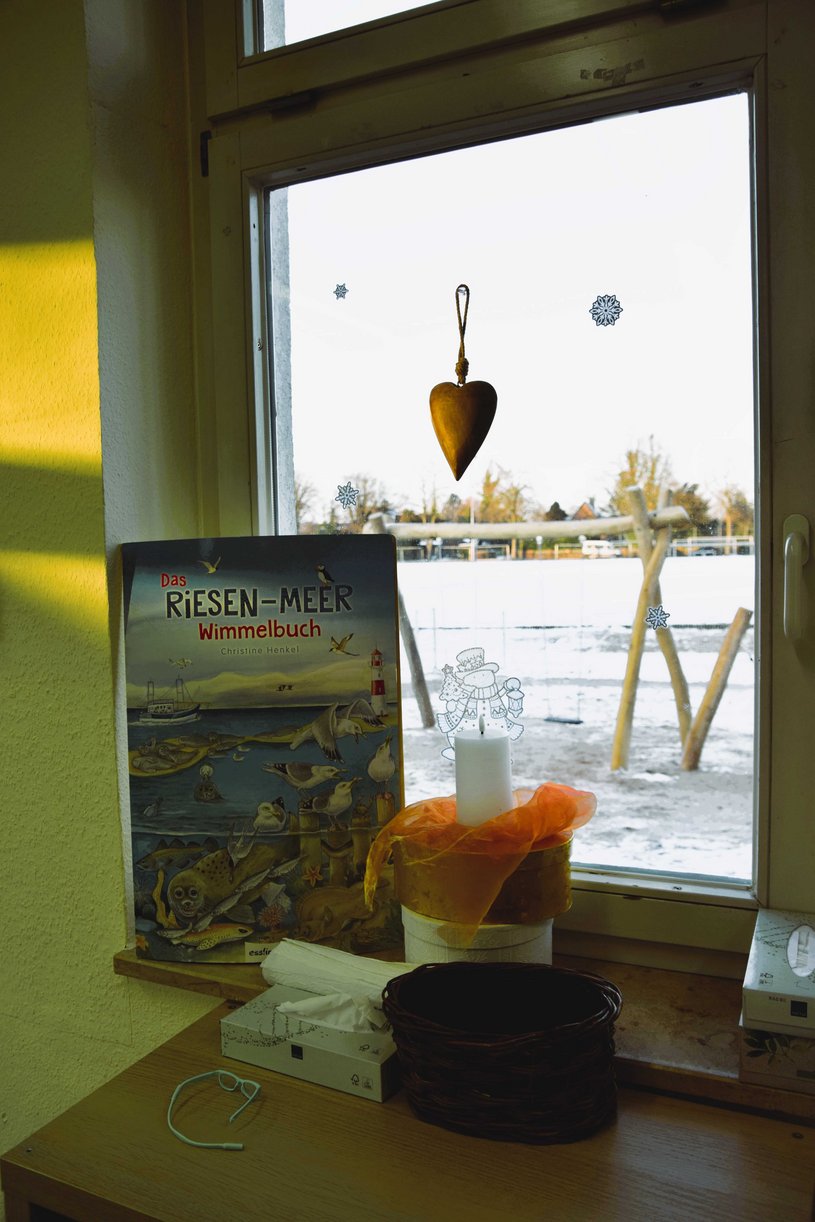 Blick aus dem Fenster auf das winterliche Draußen, im Vordergrund ein Wimmelbuch